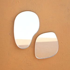 May include: Two irregular shaped, silver-framed mirrors on a brown background. The larger mirror is on the left and the smaller mirror is on the right.
