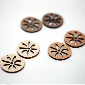May include: A collection of wooden, circular craft embellishments. Each disc features a floral design cut-out and a small hole for stringing. The wood tones vary from light to dark brown, set against a white background.