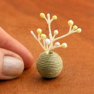 May include: A miniature white flower arrangement in a small, green, coiled rope vase.