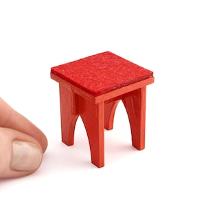 May include: Miniature red table with a square top and arched legs. The table's top has a textured surface. The small table is a vibrant red color and is designed to be a decorative item.