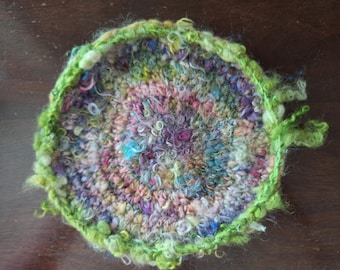 Multi-colored trivet crocheted with handspun various colored wools.  The trivet is edged with green wool with curls, lumps, and bumps.