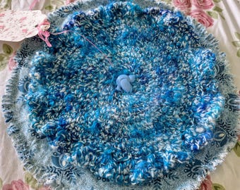Bright blues in hand-spun yarn are crocheted to make a beautiful trivet.  It is buttoned onto a circular base in a pretty teal floral.
