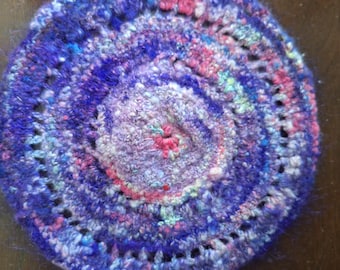 7.25 inch crocheted trivet made from purple handspun wool yarn.  The yarn has bits of pink, gray, green, and off-white in it.  Gift.