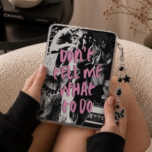 May include: A clear protective tablet case featuring a black and white collage of classical statues and figures. The text "DON'T TELL ME WHAT TO DO" is printed in bold pink letters across the center. A silver-toned charm chain with black beads, a star, and a butterfly pendant is attached to the side.
