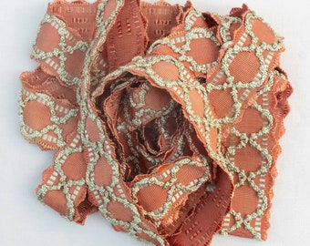 May include: A pile of terracotta-coloured fabric trim with a scalloped edge and a silver-grey geometric pattern.