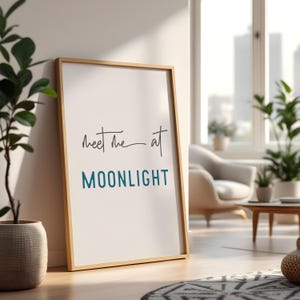 May include: A framed print with the text "Meet me at MOONLIGHT" in a light blue color. The print is in a wooden frame and is hanging on a white wall.