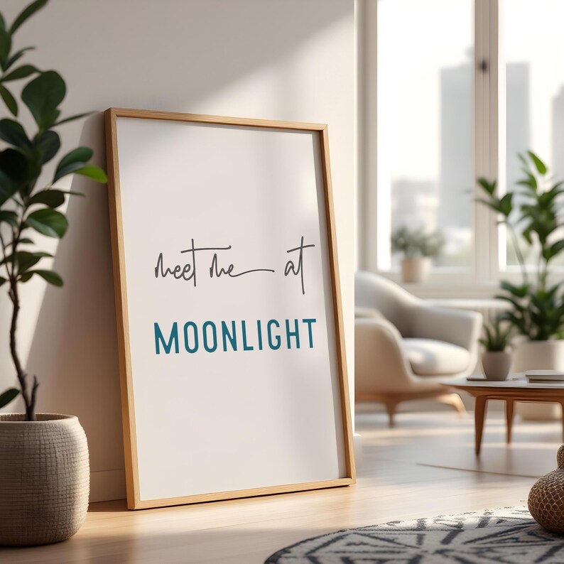 May include: A framed print with the text "Meet me at MOONLIGHT" in a light blue color. The print is in a wooden frame and is hanging on a white wall.