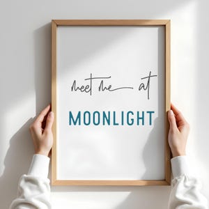 May include: A framed print with the text "Meet me at MOONLIGHT" in a light blue color. The text "Meet me" is handwritten in black.