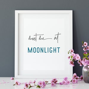 May include: White framed print with the text "Meet me at MOONLIGHT" in black and teal lettering, with pink flowers in a clear vase on a white surface.