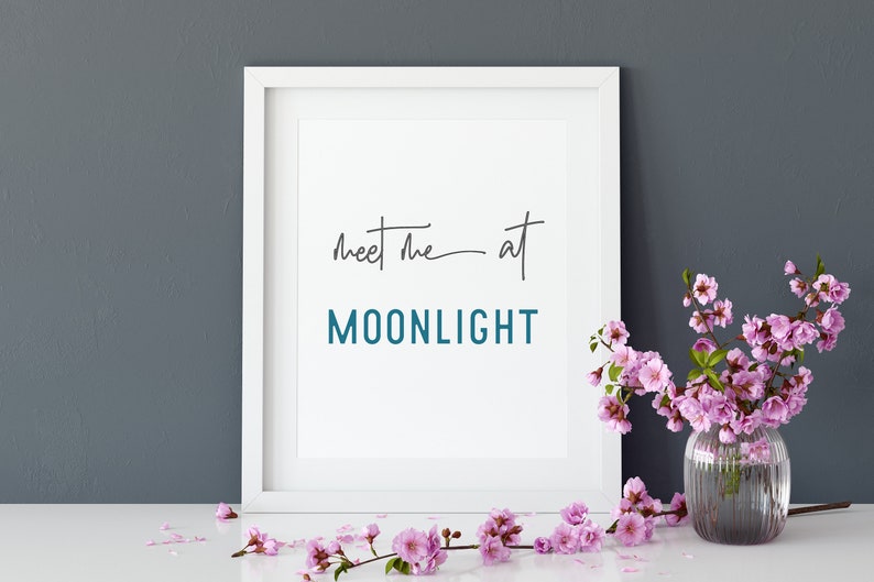 May include: White framed print with the text "Meet me at MOONLIGHT" in black and teal lettering, with pink flowers in a clear vase on a white surface.