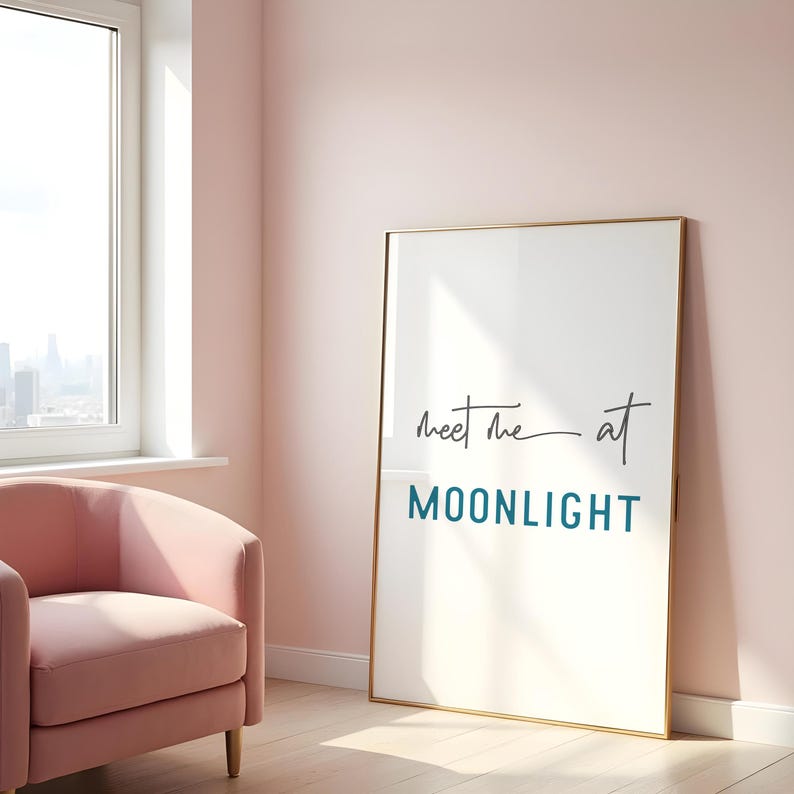 May include: A gold framed poster with the text "Meet me at MOONLIGHT" in a teal blue color. The poster is hanging on a light pink wall.