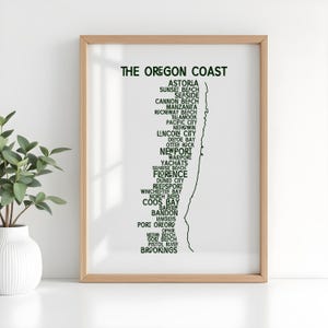 Może przedstawiać: Oprawiony wydruk z napisem "THE OREGON COAST" w kolorze zielonym, z listą nadmorskich miast. Wydruk jest w jasnej drewnianej ramie. Roślina w białym wazonie znajduje się na pierwszym planie. Wydruk przedstawia linię brzegową Oregonu.