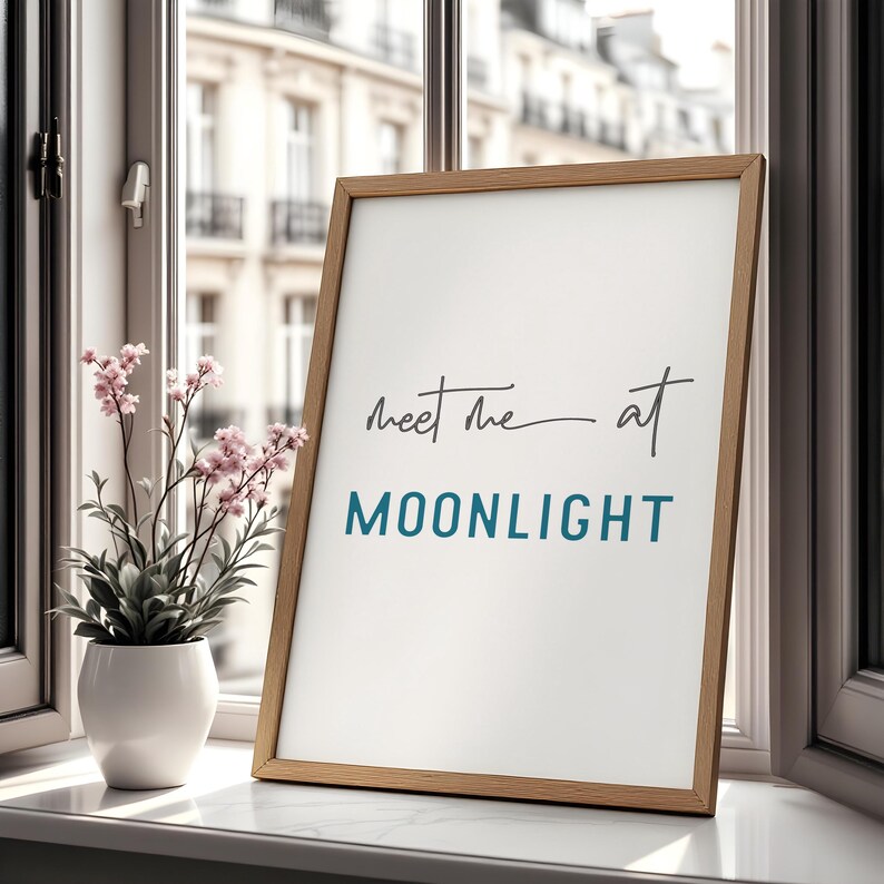 May include: A framed print with a white background and a wooden frame. The print features the text "Meet me at MOONLIGHT" in black and blue lettering.