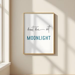 May include: A gold framed print with the text "Meet me at MOONLIGHT" in a teal blue font. The text "Meet me at" is written in cursive.