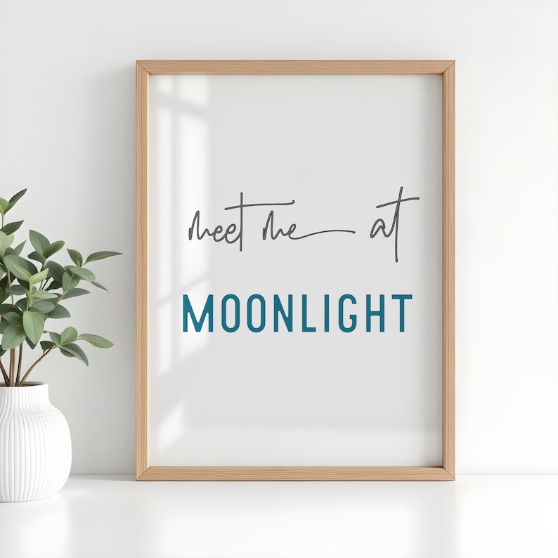 May include: A framed print with a white background and a light wood frame. The print features the text "Meet me at MOONLIGHT" in a handwritten font. The text "Meet me" is in black and "MOONLIGHT" is in teal.