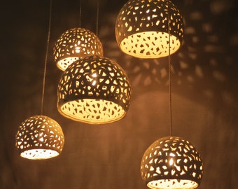 May include: Five white ceramic pendant lights with intricate cut-out designs hang from the ceiling. The lights are illuminated, casting a warm glow.