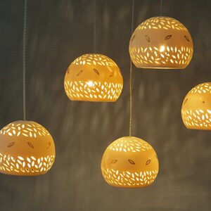 Peut inclure: Cinq lampes suspendues en c&eacute;ramique blanche avec des motifs d&eacute;coup&eacute;s complexes, suspendues au plafond et &eacute;clairant la pi&egrave;ce d'une lueur chaude.