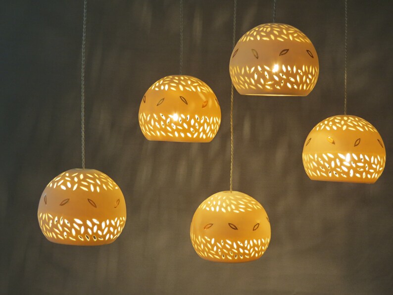 Peut inclure: Cinq lampes suspendues en c&eacute;ramique blanche avec des motifs d&eacute;coup&eacute;s complexes, suspendues au plafond et &eacute;clairant la pi&egrave;ce d'une lueur chaude.