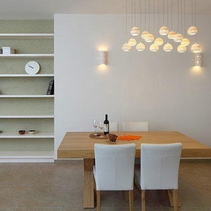 Peut inclure: Une table &agrave; manger blanche avec un plateau en bois et quatre chaises blanches. La table est dress&eacute;e avec une bouteille de vin, deux verres &agrave; vin et un bol de fruits. La pi&egrave;ce est d&eacute;cor&eacute;e dans un style moderne avec des murs blancs et une biblioth&egrave;que blanche.