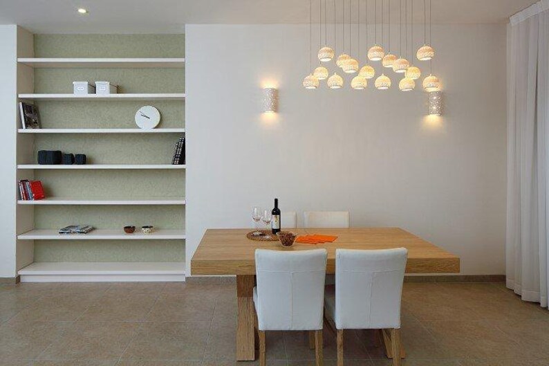 Peut inclure: Une table &agrave; manger blanche avec un plateau en bois et quatre chaises blanches. La table est dress&eacute;e avec une bouteille de vin, deux verres &agrave; vin et un bol de fruits. La pi&egrave;ce est d&eacute;cor&eacute;e dans un style moderne avec des murs blancs et une biblioth&egrave;que blanche.