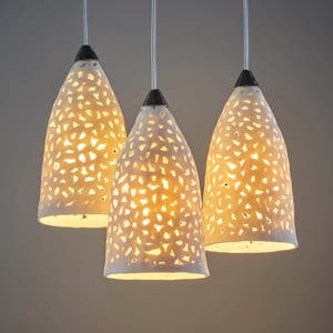 Op de afbeelding: Drie witte keramische hanglampen met ingewikkelde uitgesneden ontwerpen, hangend aan een plafond.