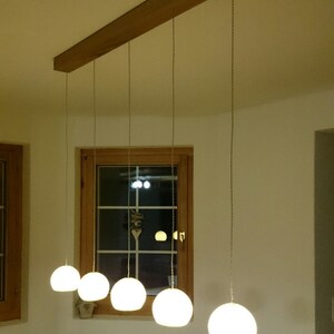 May include: A wooden ceiling fixture with five white globe-shaped pendant lights hanging from it. The lights are hanging over a wooden table with a white chair in the foreground.