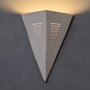 May include: A white triangular wall sconce with a geometric pattern of cutouts. The sconce is lit from within, casting a warm glow.