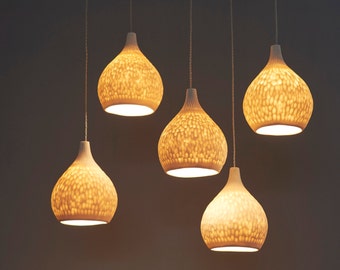 May include: Five white ceramic pendant lights with a textured surface hang from the ceiling. The lights are turned on and emit a warm glow.
