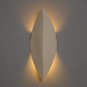 Op de afbeelding: Een witte keramische wandlamp in de vorm van een blad met een warm licht dat uit het midden straalt.