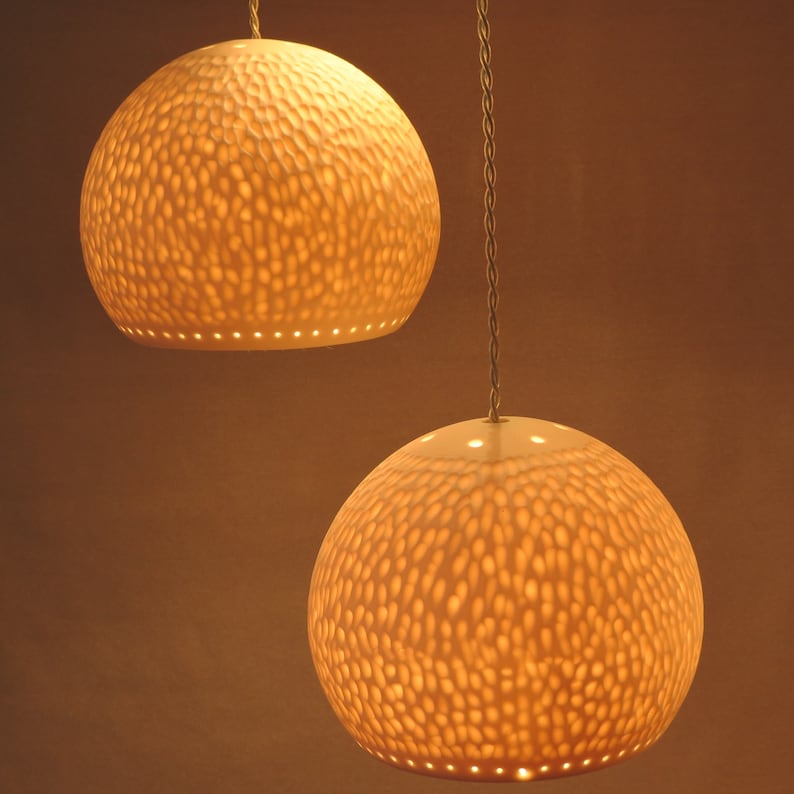 May include: Two white ceramic pendant lights with a textured, honeycomb-like design. The lights are illuminated and cast a warm glow.