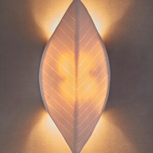 May include: A white ceramic leaf-shaped wall sconce with a light inside, casting a warm glow on the wall.