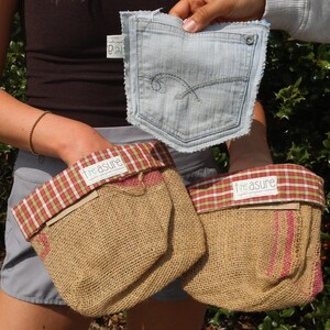 May include: Three burlap pouches with red and white plaid trim and the word "treasure" on a white label. A denim pocket is held above the pouches. The pouches are made of a natural fiber material.