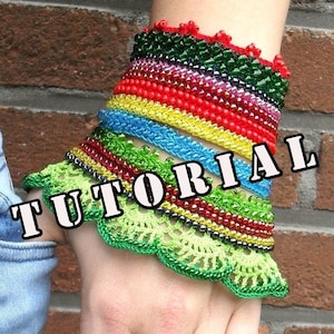 Op de afbeelding: Een kleurrijke kralen armband met een groene gehaakte rand. De armband is gemaakt van meerdere strengen kralen in verschillende kleuren, waaronder rood, geel, blauw, groen en zwart. Het woord "TUTORIAL" is over de afbeelding gelegd.