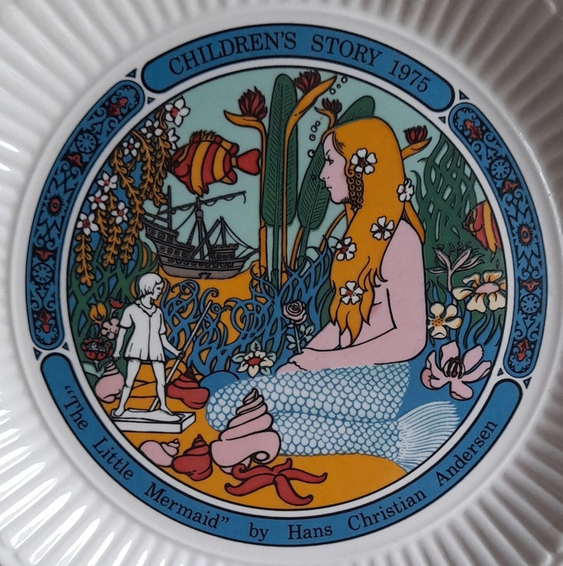 May include: A white ceramic plate with a colorful illustration of a mermaid with long blonde hair, a ship, and a small boy. The plate has the text "Children's Story 1975" and "The Little Mermaid" by Hans Christian Andersen.