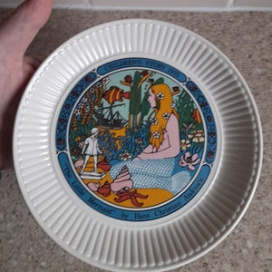 May include: A white ceramic plate with a blue border and a colorful illustration of a mermaid and a ship. The plate reads "Children's Story 1975" and "The Little Mermaid" by Hans Christian Andersen.
