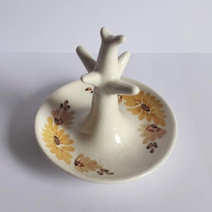 Puede incluir: Porta anillos de cerámica blanca con un soporte en forma de árbol y un plato para anillos decorado con girasoles amarillos y marrones.