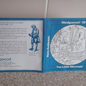 May include: A blue and white ceramic plate with a black and white illustration of a mermaid from Hans Christian Andersen's The Little Mermaid. The plate is part of a series of children's stories from Wedgwood, 1975.