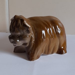 May include: A brown ceramic figurine of a Highland cow with a shaggy coat. The figurine is detailed with a textured surface and a realistic appearance.