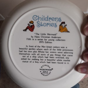May include: White ceramic plate with a colorful illustration of two children reading books. The plate is part of a series called "Children's Stories" and features the story "The Little Mermaid" by Hans Christian Andersen. The plate is from the 1975 edition.