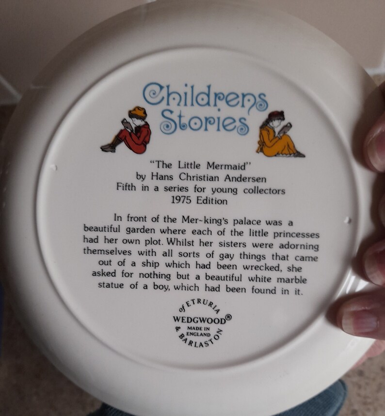 May include: White ceramic plate with a colorful illustration of two children reading books. The plate is part of a series called "Children's Stories" and features the story "The Little Mermaid" by Hans Christian Andersen. The plate is from the 1975 edition.