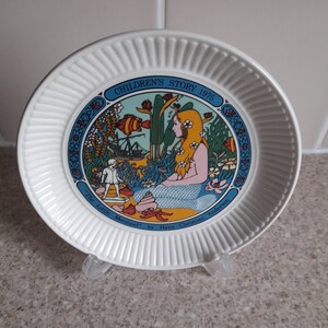 May include: A white ceramic plate with a blue and yellow illustration of a mermaid and a ship. The plate has the text "Children's Story 1975" and "The Little Mermaid by Hans Christian Andersen" around the illustration.