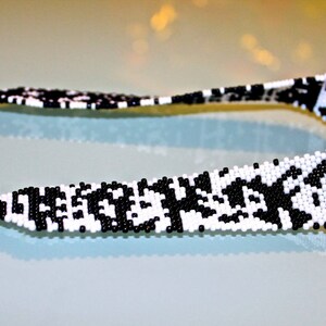 May include: A black and white beaded necklace with a geometric pattern. The necklace is made of small, round beads and has a silver clasp.