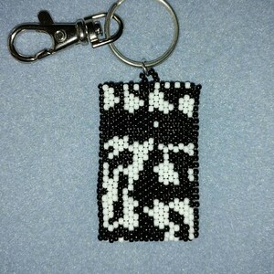 May include: Black and white beaded keychain with a silver key ring and clasp. The beads are arranged in a geometric pattern.