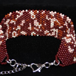 May include: A beaded bracelet with a brown, pink, and white geometric pattern. The bracelet has a silver clasp.