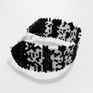 May include: Black and white beaded bracelet with a geometric pattern. The bracelet is made of small, round beads and has a silver clasp.