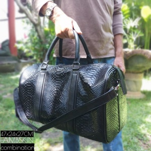 Puede incluir: Bolsa de viaje de cuero negro con estampado de piel de serpiente. La bolsa tiene un asa superior y una correa para el hombro. La bolsa mide 47x24x27 cm. Combinación de piel de cordero.
