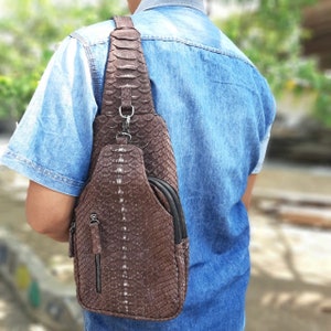 May include: A brown leather crossbody bag with a snakeskin pattern. The bag has a zipped pocket on the front and a strap that goes over the shoulder.