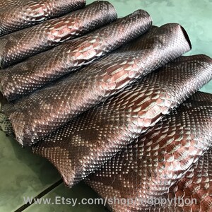 May include: A stack of six brown and silver python skins. The skins are folded in half and have a scaly texture.