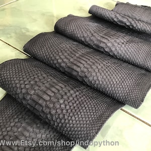 Könnte beinhalten: Nahaufnahme einer Stapel schwarzer Python-Lederhäute. Das Leder hat eine strukturierte, schuppige Textur.