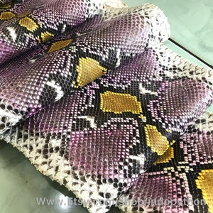 以下が含まれることがあります： 紫、白、金色のパイソンレザーの断片をクローズアップ。レザーは積み重ねられており、鱗がはっきりと見えます。